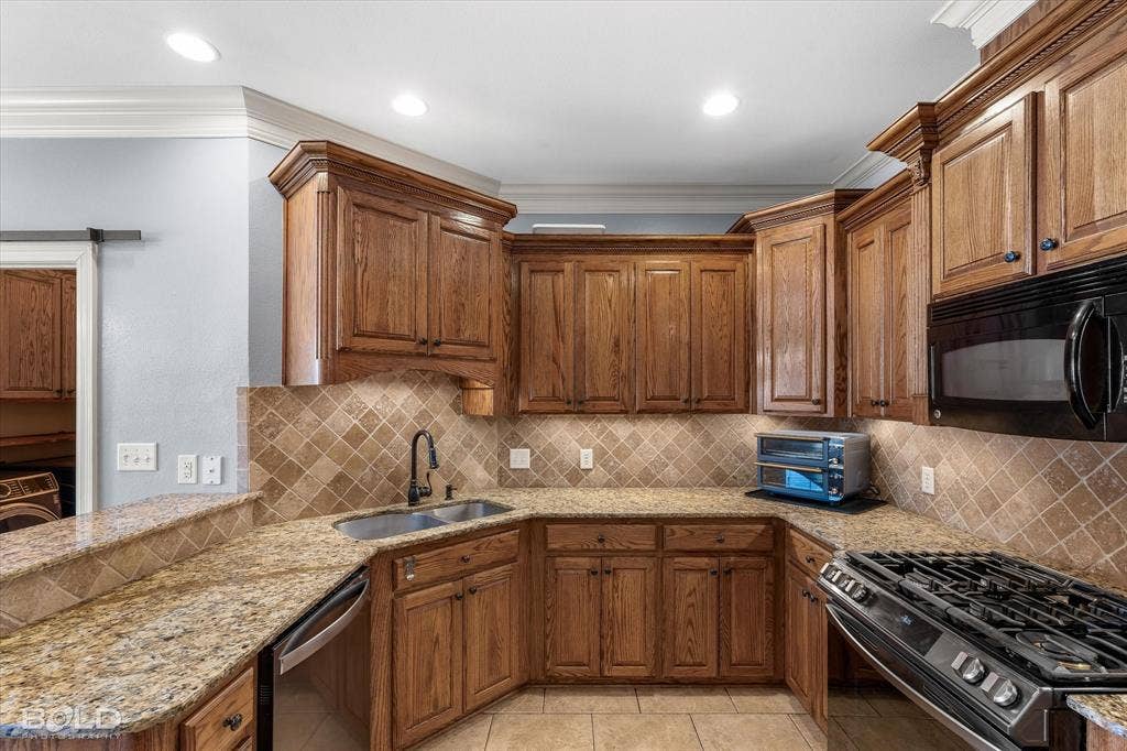 Kitchen featuring stained wood cabinetry, stone-surface countertops, stone tile backsplash, crown molding, and stainless steel appliances