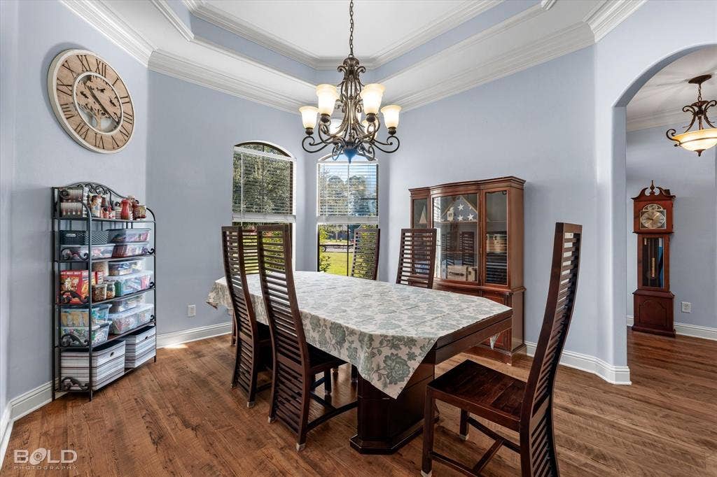 Dining area featuring a recessed tray ceiling, wood-finish flooring, multi-light decorative chandelier, and arched wall openings