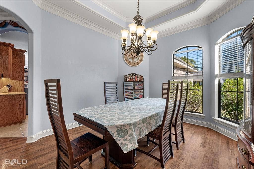 Tray ceiling, multi-light chandelier, wood-finish flooring, and arched windows