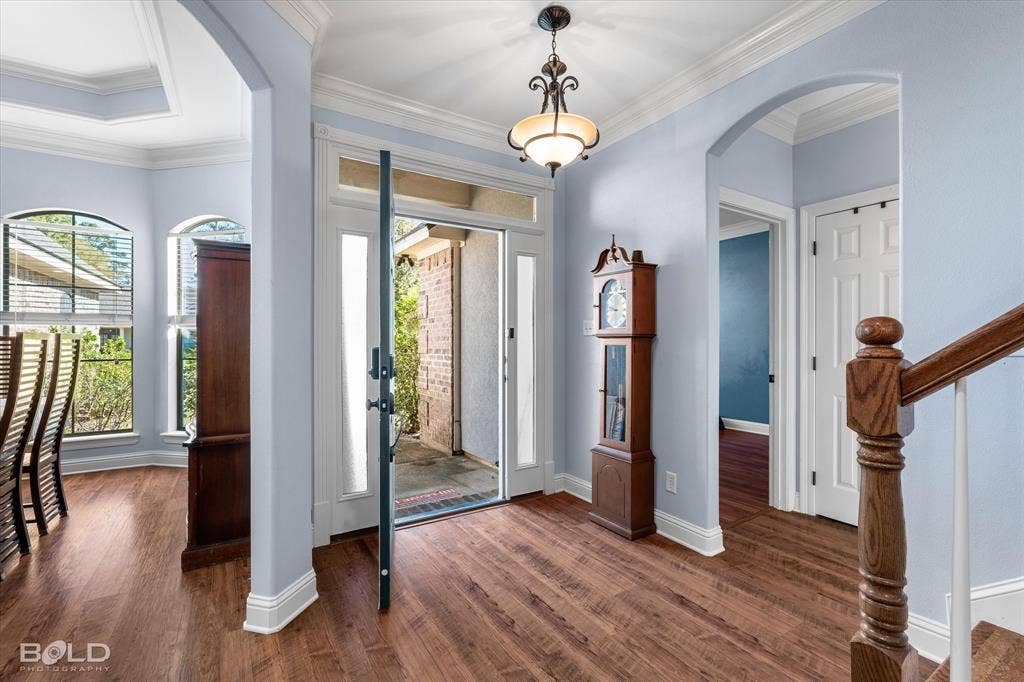 Entryway featuring wood-finish flooring, an arched entryway, transom windows above the door, crown molding, and a traditional pendant light fixture