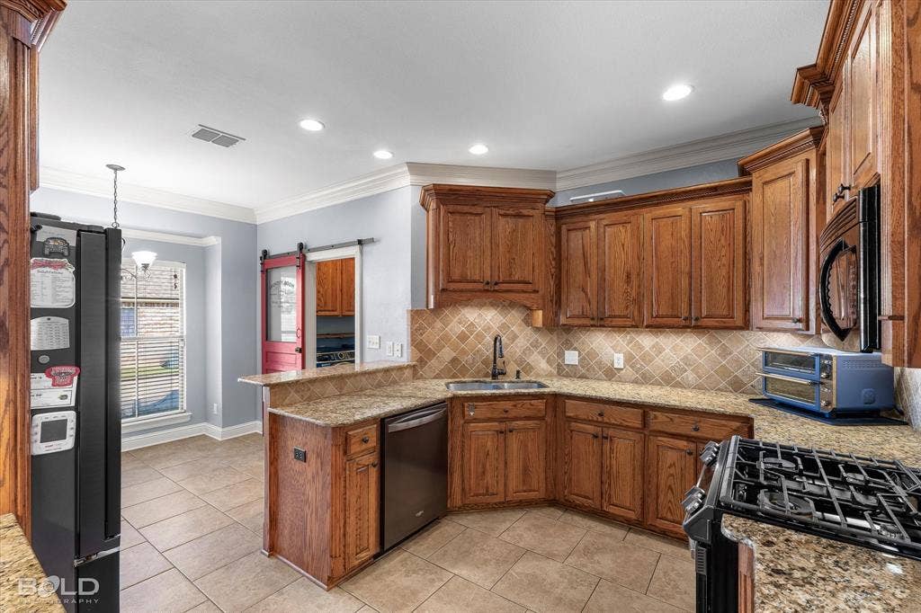 Kitchen featuring stained wood cabinetry, stone-finish countertops, diagonal tile backsplash, ceramic tile flooring, and a sliding barn door entry