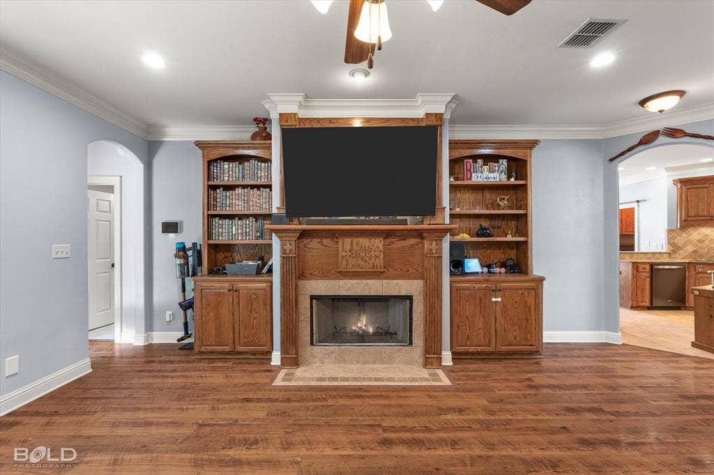 Living area featuring wood-finish flooring, custom built-in wood cabinetry with integrated shelving, and a central fireplace with stone-tile surround