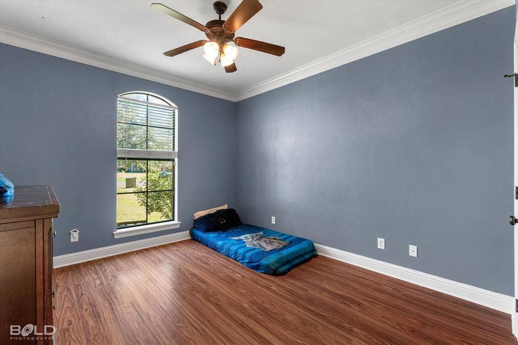 Room featuring wood-finish flooring, an arched window, crown molding, and a ceiling fan with integrated lighting