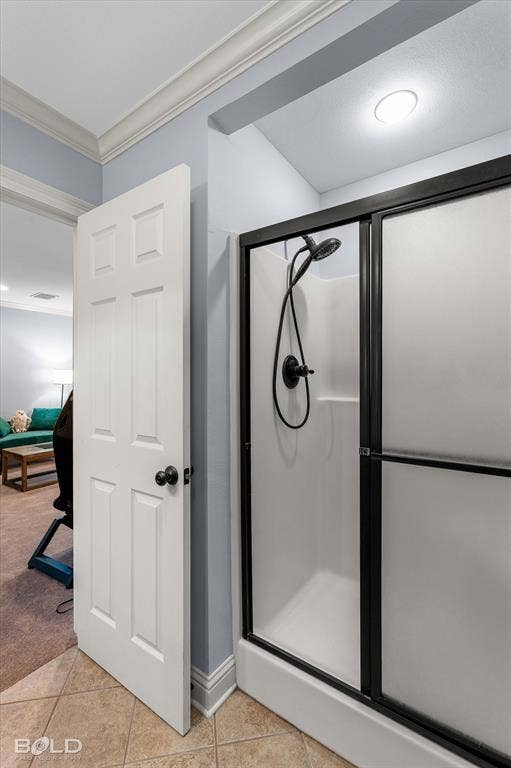 Shower stall with a black-framed sliding glass door, handheld shower fixture, matte black hardware, crown molding, and neutral tile flooring