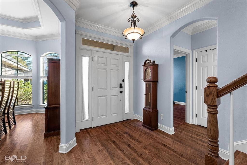 Entryway featuring wood-finish flooring, vaulted ceiling, arched architectural detailing, crown molding, and a paneled front door with sidelights and transom window