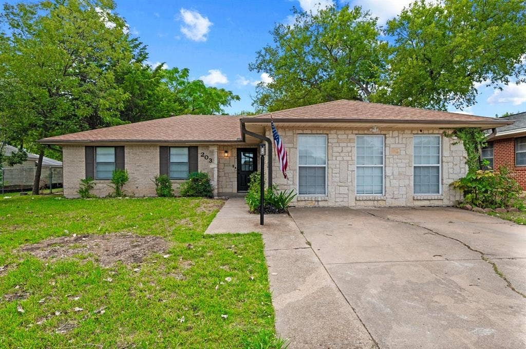 203 Evelyn Street, DeSoto, TX 75115 Single-story residence featuring a light-toned brick and stone masonry facade, horizontal roofline, expansive front lawn, and concrete driveway
