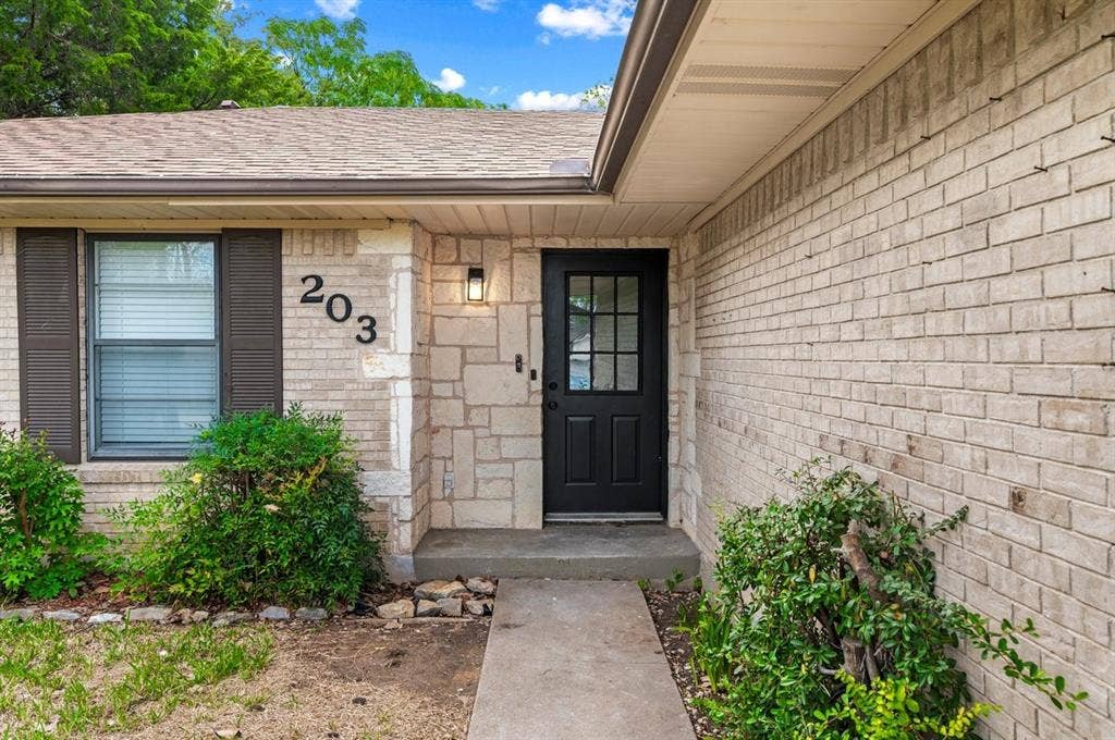 203 Evelyn Street, DeSoto, TX 75115 Exterior facade featuring light-toned brick and stone masonry, dark-framed multi-pane front door, and dark shutters