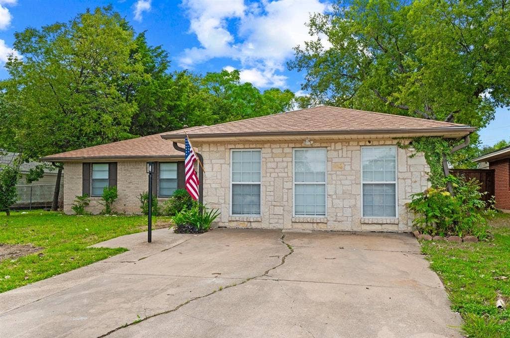 203 Evelyn Street, DeSoto, TX 75115 Single-story exterior featuring a natural stone facade, hip roof with composition shingles, multiple vertical rectangular windows, and a concrete driveway