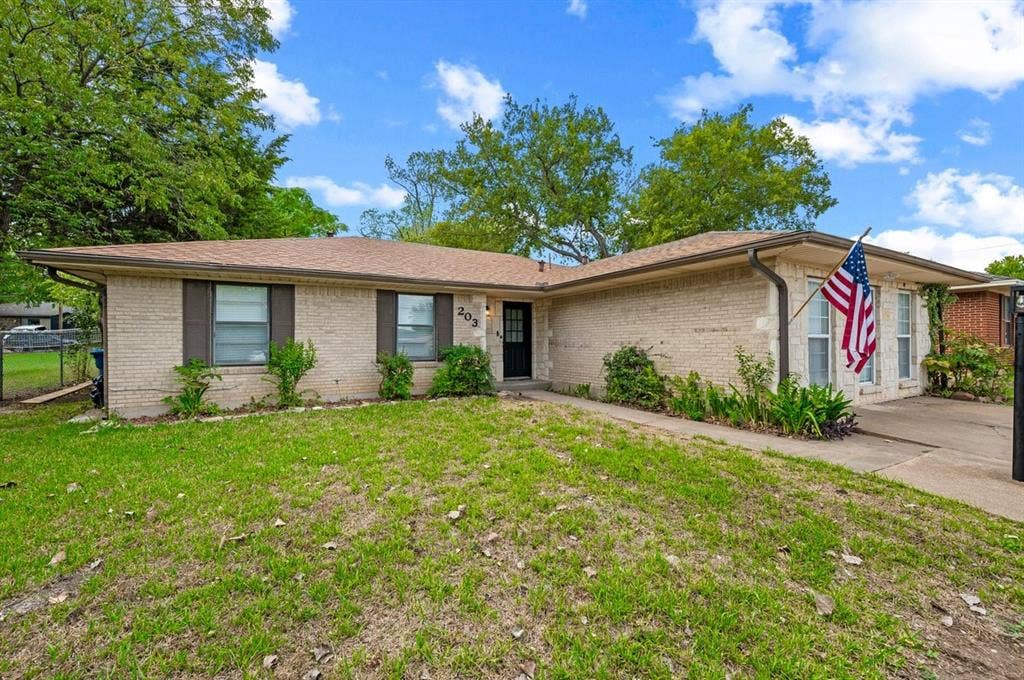 203 Evelyn Street, DeSoto, TX 75115 Single-story exterior featuring light-toned brick masonry, a low-pitched roof, dark shutters, and a concrete driveway