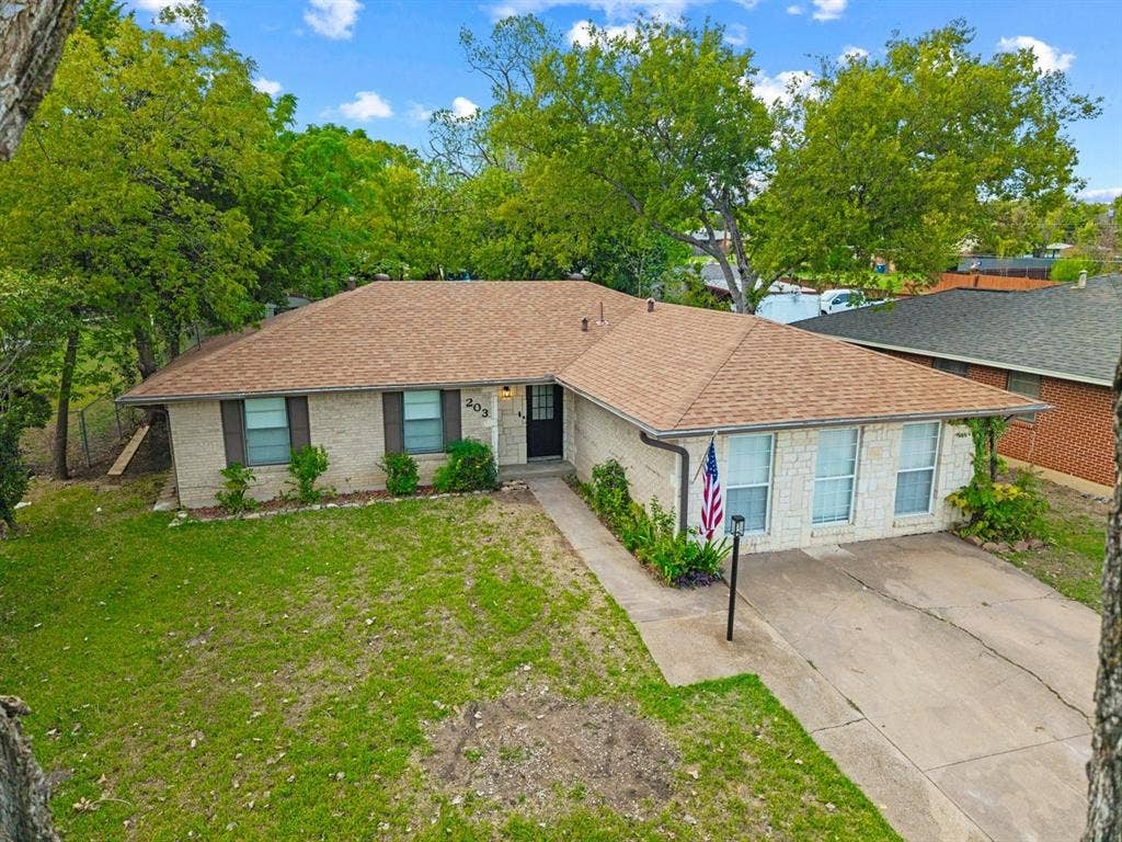 203 Evelyn Street, DeSoto, TX 75115 Single-story residence featuring a light-toned brick facade, hipped roof, concrete driveway, and mature landscaping