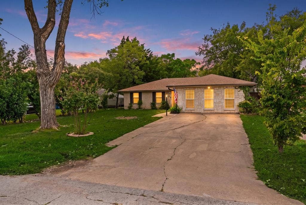 203 Evelyn Street, DeSoto, TX 75115 Single-story exterior featuring light-toned stone masonry, a low-pitch roof, symmetrical window placement, and an expansive concrete driveway