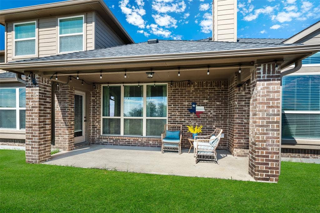 13176 Franklin Lane, Talty, TX 75126 Covered concrete patio featuring brick exterior columns, multi-pane windows, and a shingle roof