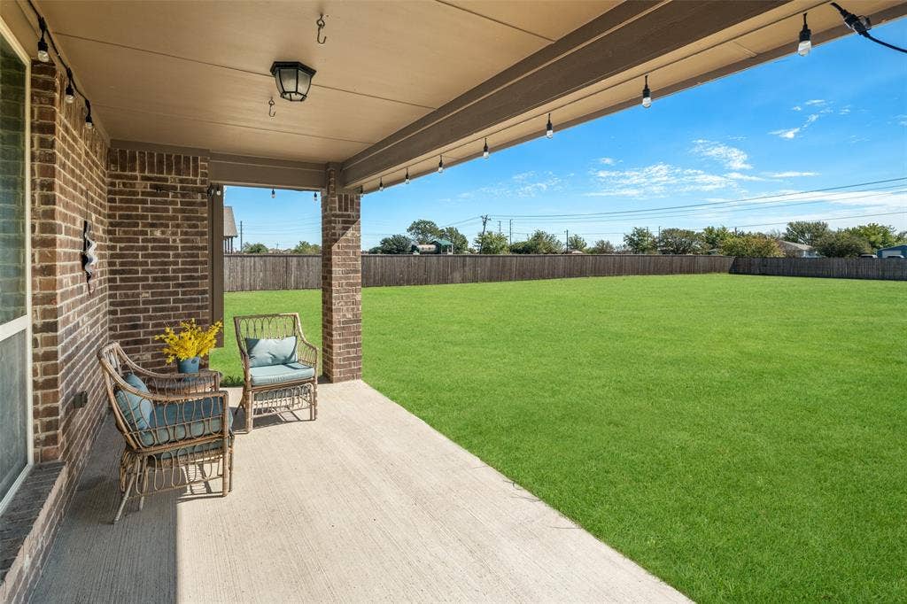 13176 Franklin Lane, Talty, TX 75126 Covered concrete patio featuring brick exterior columns, exterior wall-mounted lighting, and an expansive level backyard enclosed by wood fencing