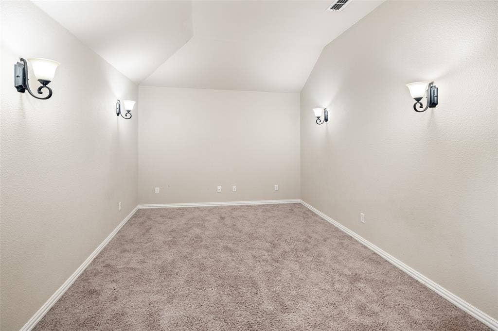 13176 Franklin Lane, Talty, TX 75126 Neutral-toned interior space featuring vaulted ceilings, wall-to-wall carpeting, and four decorative wall-mounted light fixtures