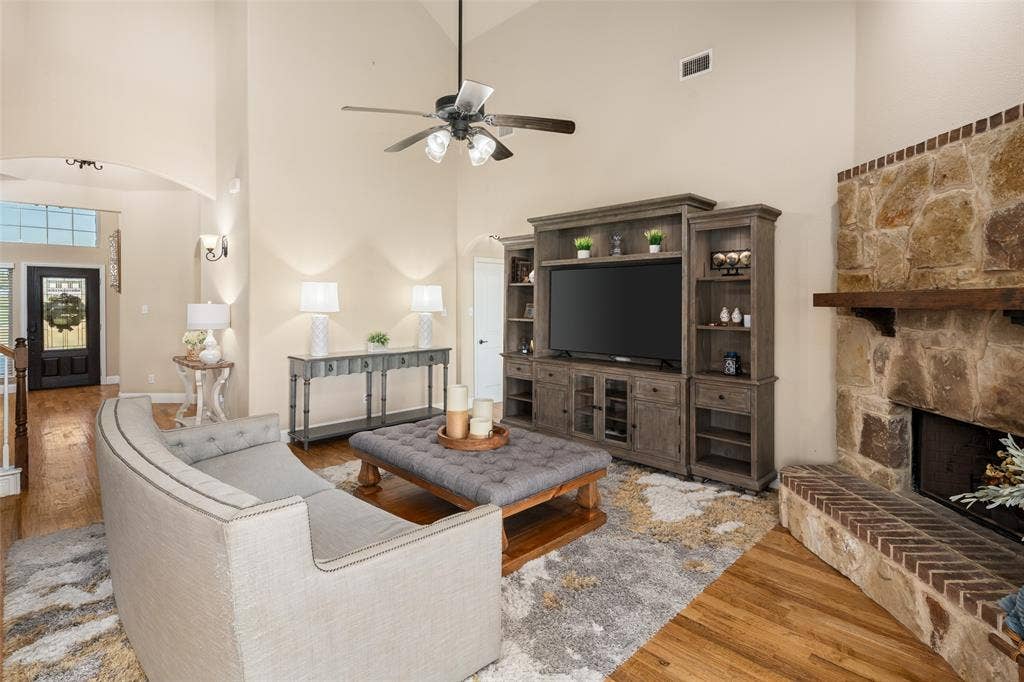13176 Franklin Lane, Talty, TX 75126 Vaulted ceiling featuring a ceiling fan, floor-to-ceiling stone fireplace with a wood mantel, brick hearth, and wood-finish flooring