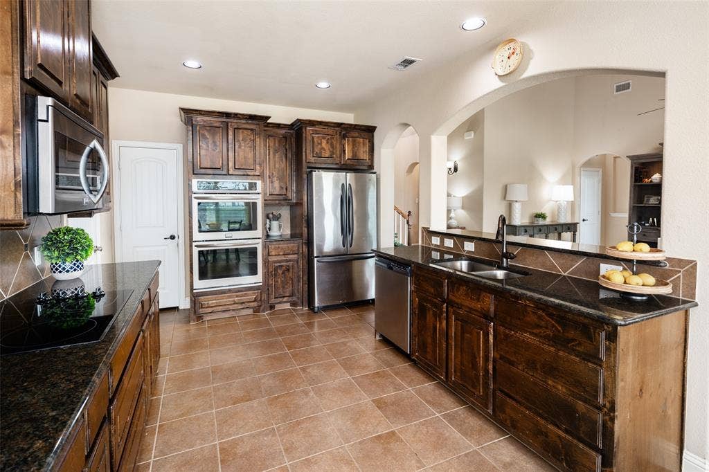13176 Franklin Lane, Talty, TX 75126 Kitchen featuring dark-stained cabinetry, integrated stainless steel appliances, dual wall ovens, dark stone countertops, and tile flooring