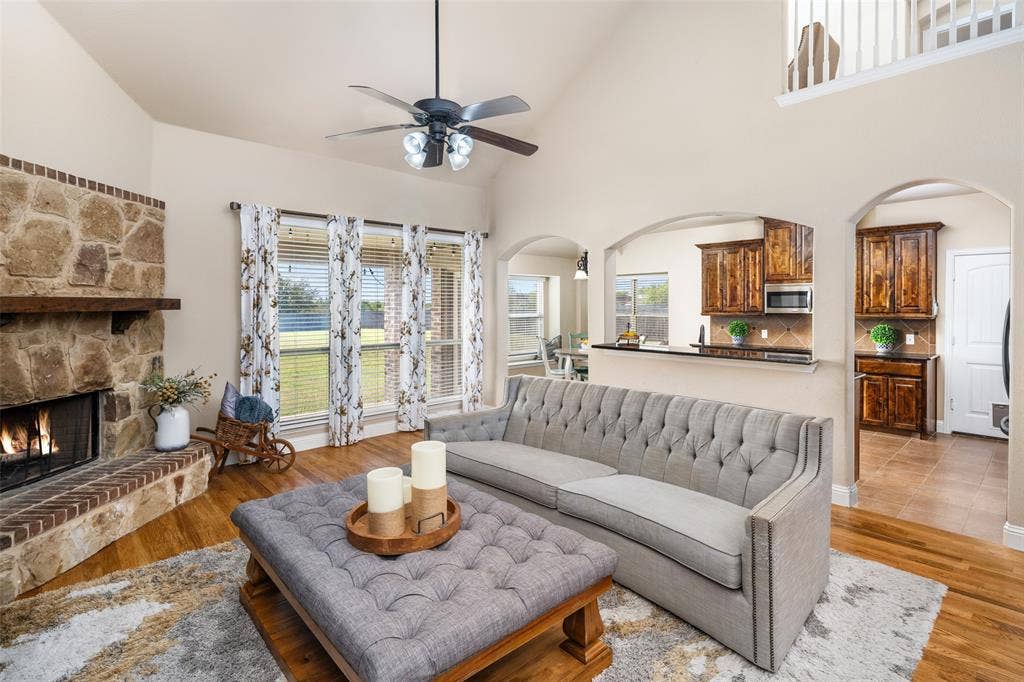 13176 Franklin Lane, Talty, TX 75126 Vaulted ceilings, floor-to-ceiling stone fireplace with a timber mantel, wood-finish flooring, and arched architectural openings