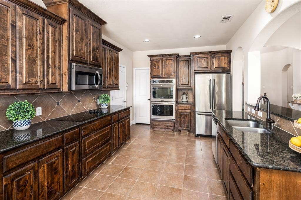 13176 Franklin Lane, Talty, TX 75126 Kitchen featuring dark wood cabinetry, stone countertops, tiled backsplash, stainless steel double wall ovens, and stainless steel refrigerator