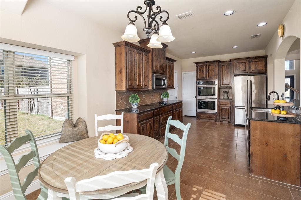 13176 Franklin Lane, Talty, TX 75126 Kitchen featuring dark-stained wood cabinetry, stone countertops, tiled backsplash, integrated stainless steel appliances including a built-in double oven, and tile flooring