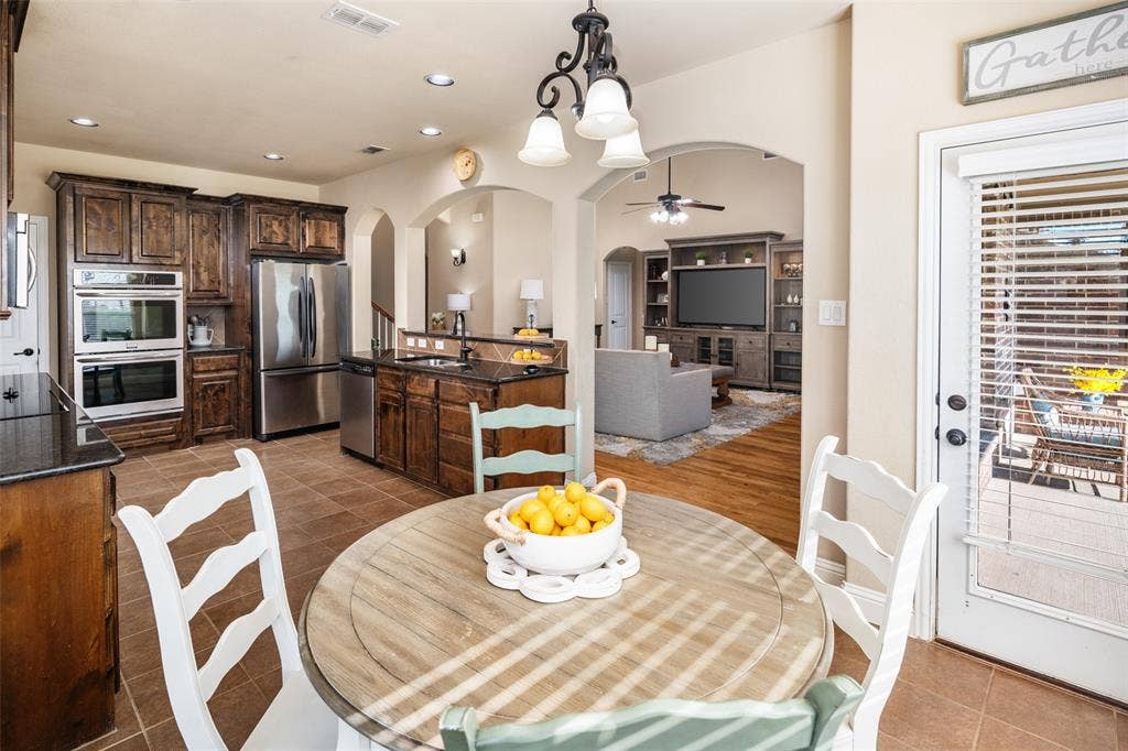 13176 Franklin Lane, Talty, TX 75126 Kitchen featuring dark wood cabinetry, stainless steel appliances, built-in double oven, dark stone countertops, and tile flooring with recessed lighting