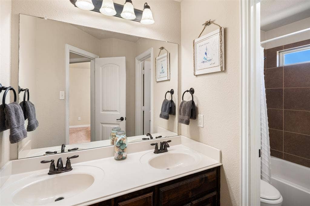 13176 Franklin Lane, Talty, TX 75126 Double vanity featuring dark wood-finish cabinetry, solid-surface countertop with integrated dual sinks, oil-rubbed bronze fixtures, and large rectangular wall mirror