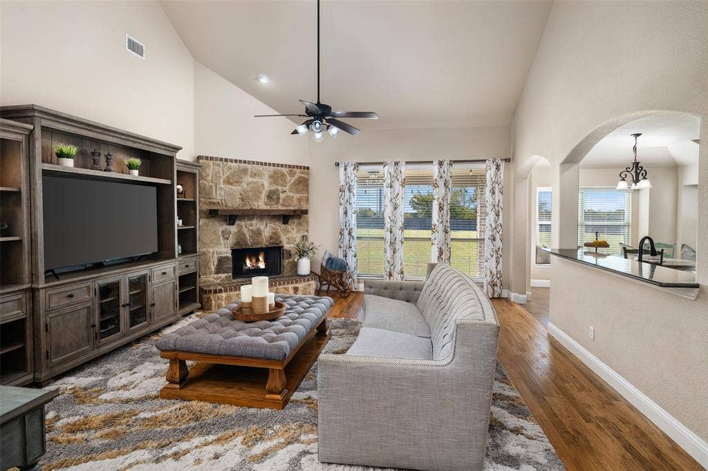 13176 Franklin Lane, Talty, TX 75126 Vaulted ceilings with a stone-surround fireplace, built-in cabinetry, wood-finish flooring, and a breakfast bar with an arched pass-through
