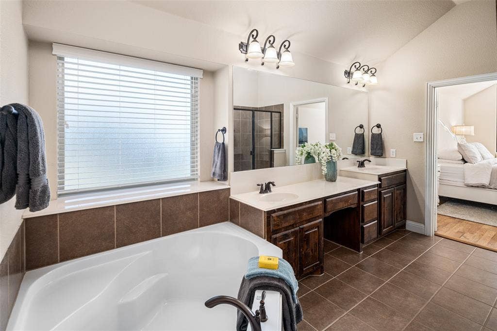 13176 Franklin Lane, Talty, TX 75126 Bathroom featuring a soaking tub with tile surround, dual-sink vanity with dark-stained cabinetry, large vanity mirrors, and ceramic tile flooring