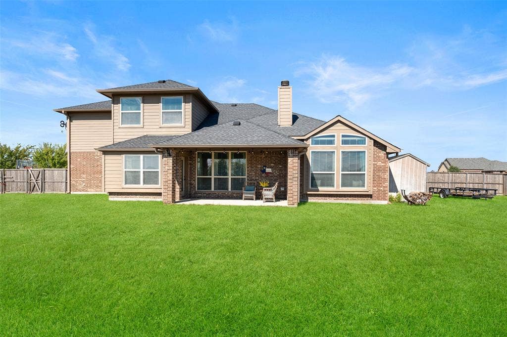 13176 Franklin Lane, Talty, TX 75126 Two-story residence featuring a brick and siding exterior, a covered rear patio, a chimney, and an expansive lawn enclosed by wood fencing