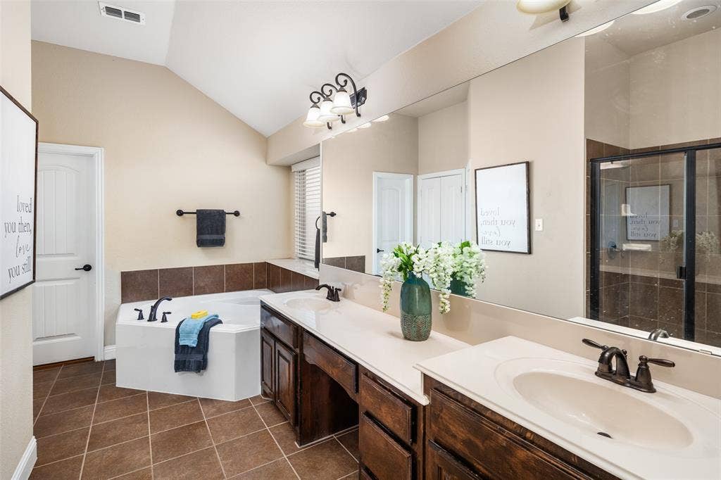 13176 Franklin Lane, Talty, TX 75126 Bathroom featuring vaulted ceilings, dual-sink vanity with dark wood cabinetry, soaking tub with tile surround, walk-in shower with glass enclosure, and tile flooring