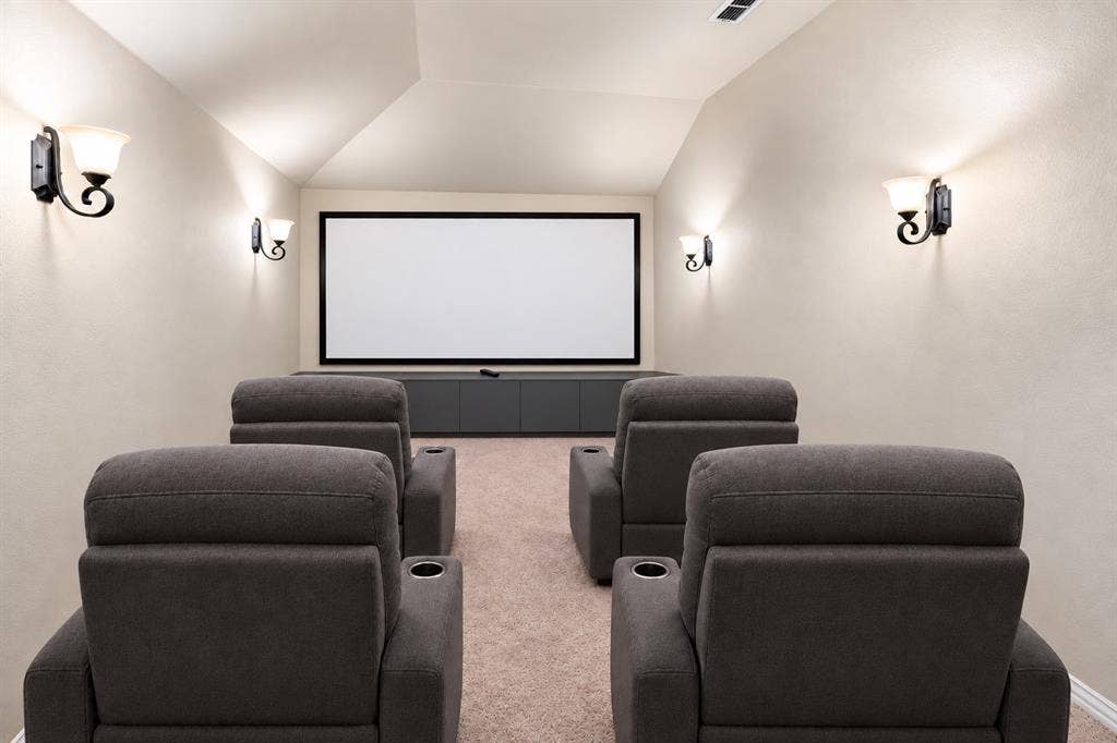13176 Franklin Lane, Talty, TX 75126 AI STAGED - Dedicated media room featuring a mounted projection screen, built-in lower cabinetry, wall-mounted sconce lighting, and a vaulted ceiling