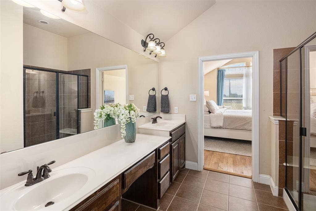 13176 Franklin Lane, Talty, TX 75126 Dual-sink vanity with solid-surface countertop and dark-finish cabinetry, expansive wall-to-wall mirror, tiled flooring, and a glass-enclosed shower with tiled surround