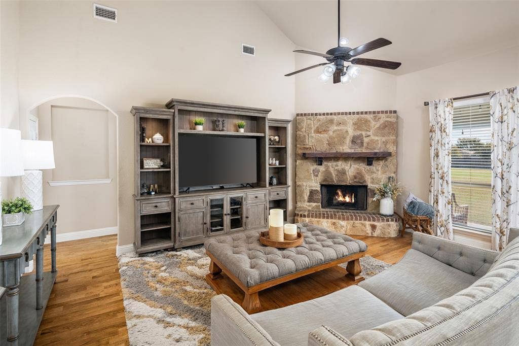13176 Franklin Lane, Talty, TX 75126 Living area featuring a vaulted ceiling, stone-surround corner fireplace with a wooden mantel, wood-finish flooring, and built-in cabinetry