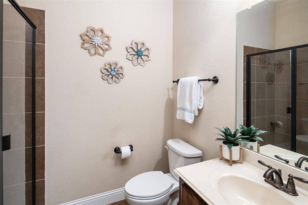 13176 Franklin Lane, Talty, TX 75126 Bathroom featuring a vanity with an integrated countertop sink, dark finish faucet hardware, a large wall-mounted mirror, and a walk-in shower with tiled surround and black frame