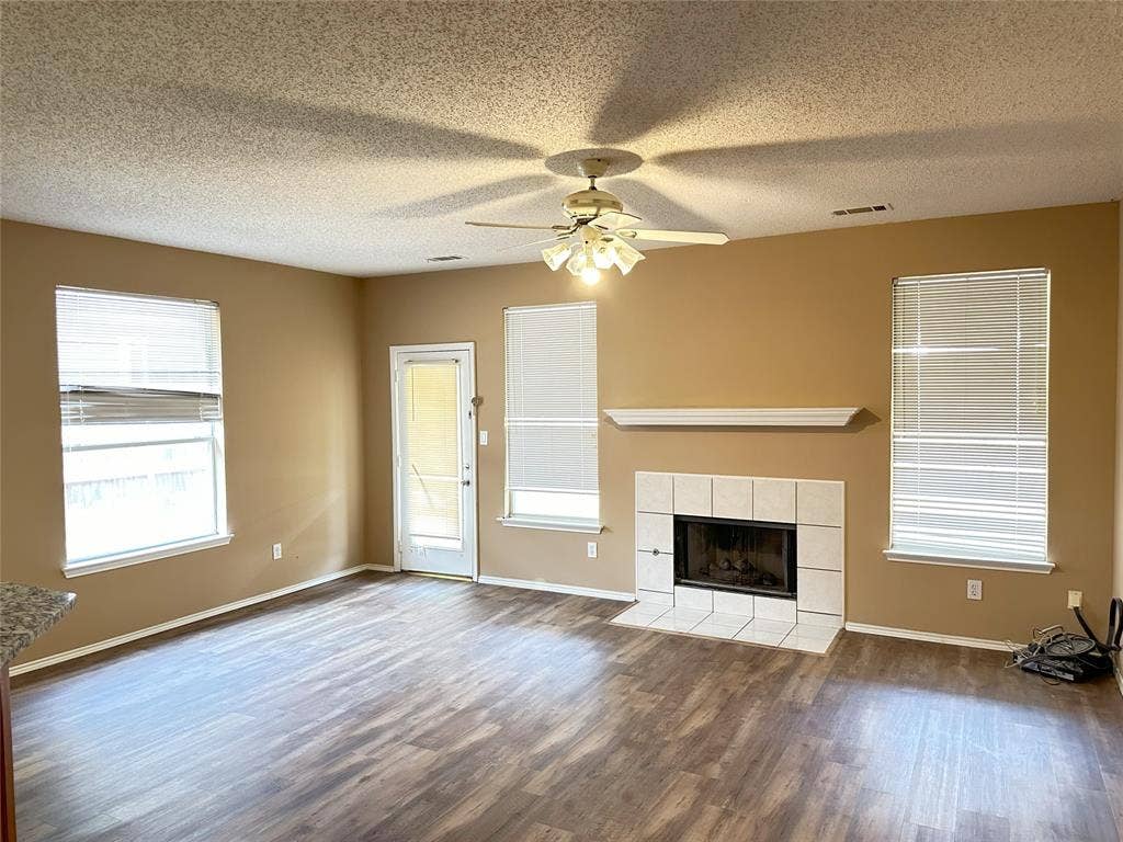 7800 Crestview Drive, Plano, TX 75024 Spacious living area featuring wood-finish flooring, a tiled fireplace with mantel, and multiple windows with blinds