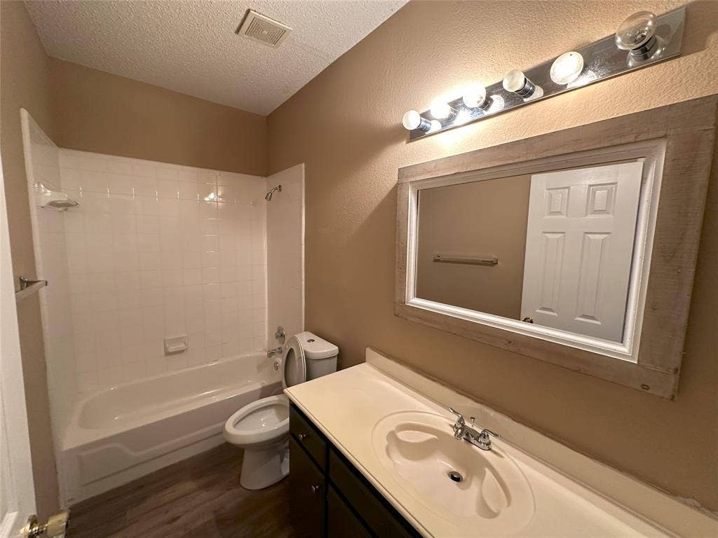 7800 Crestview Drive, Plano, TX 75024 Bathroom with an integrated sink vanity, wood-finish flooring, full bathtub with shower, and a framed wall mirror