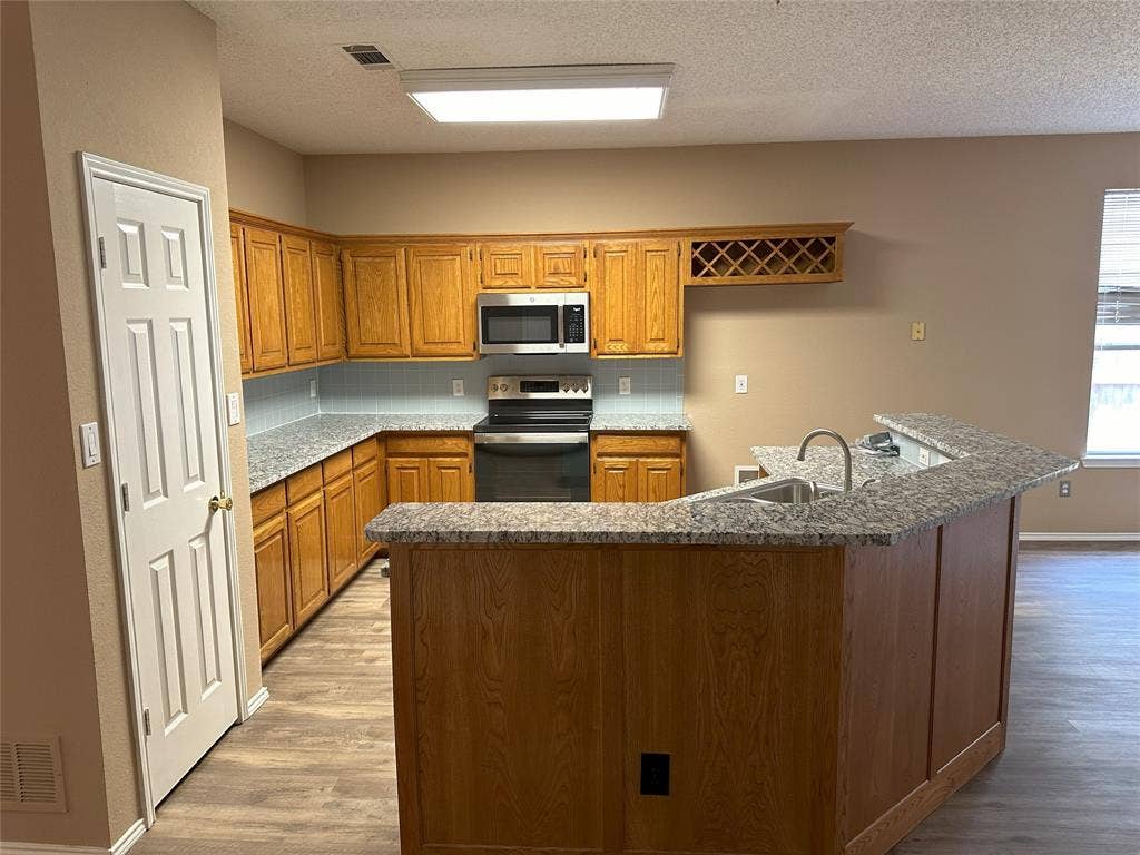 7800 Crestview Drive, Plano, TX 75024 Kitchen featuring wood-finish cabinetry, granite-style countertops, stainless steel appliances, a built-in wine rack, and wood-finish flooring