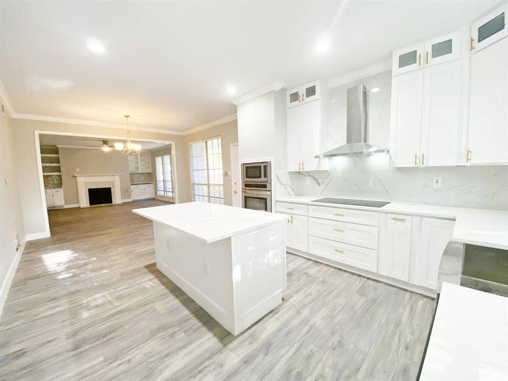 1700 Shiprock Drive, Plano, TX 75025 Kitchen featuring backsplash, light hardwood / wood-style flooring, stainless steel appliances, wall chimney range hood, and white cabinetry