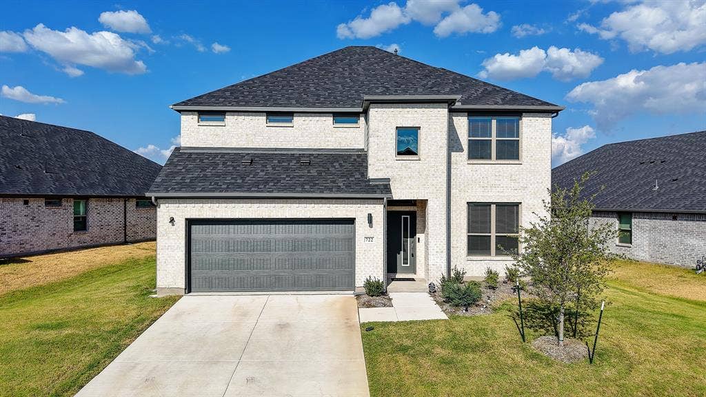 Contemporary two-story residence featuring light-colored brick, a dark shingle roof, a two-car garage with a dark panel door, and a concrete driveway