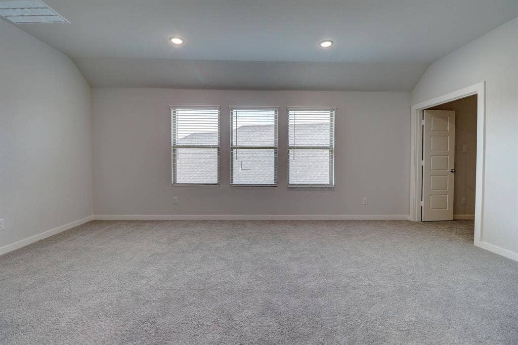 Spacious room featuring gray carpeting, multiple windows with blinds, recessed ceiling lighting, and an architectural vaulted ceiling detail