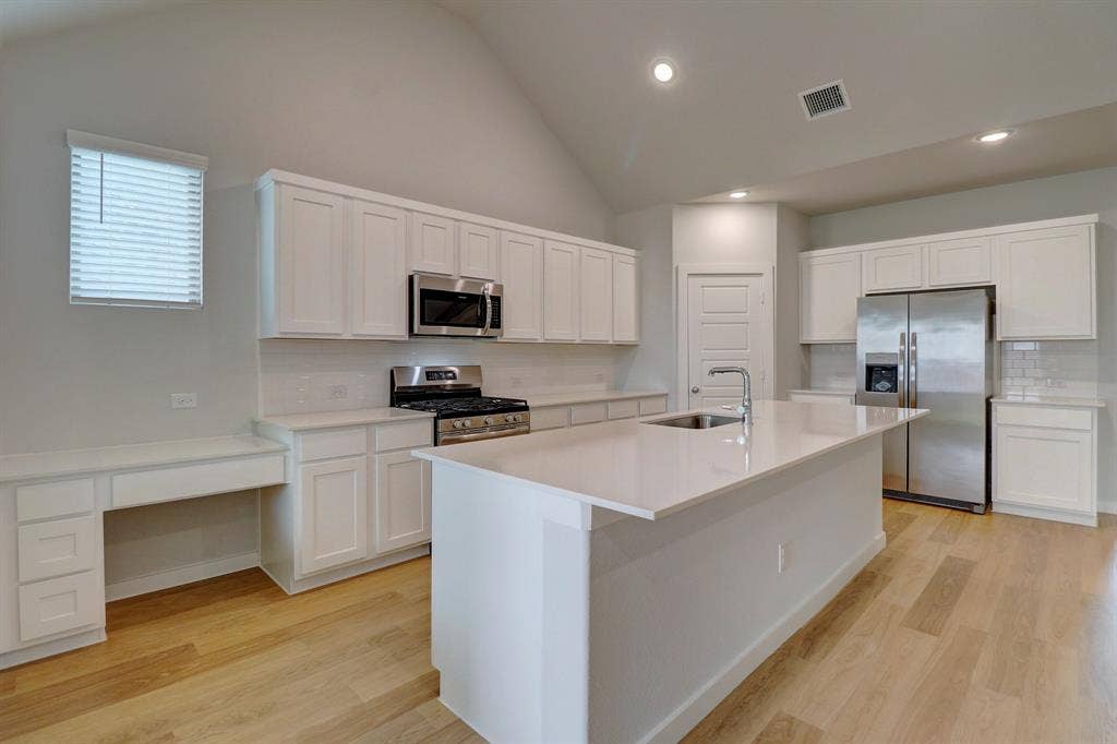 Kitchen featuring wood-finish flooring, vaulted ceiling, white cabinetry, stainless steel appliances, and a central island with an undermount sink