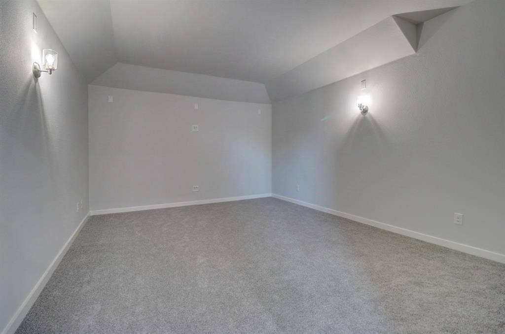 Vaulted ceiling with sconce lighting and neutral-toned carpet