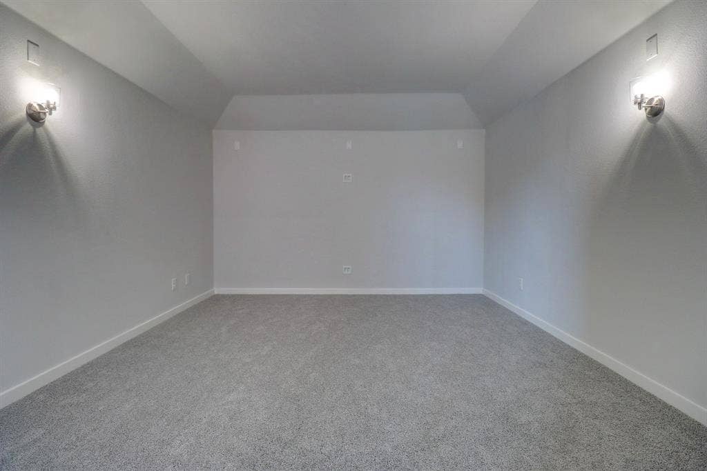 Recessed wall panel, sconce lighting, vaulted ceiling, and gray carpet