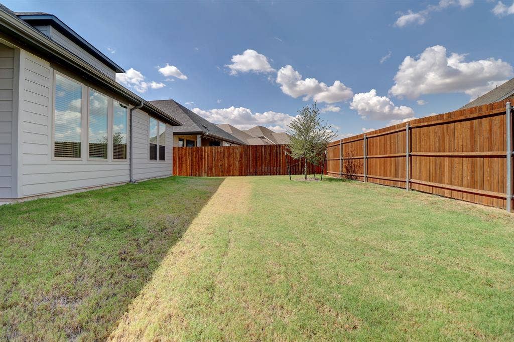 Expansive backyard featuring a privacy fence, established lawn, and a young tree
