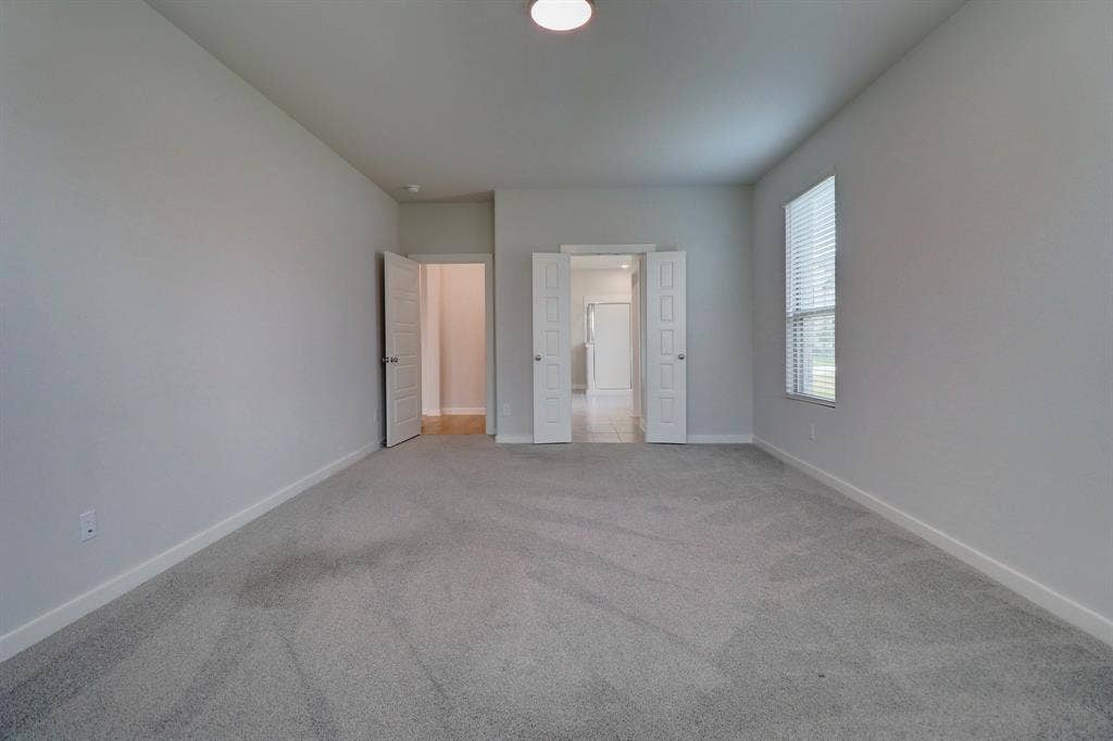 Spacious room featuring light gray carpeting, neutral wall finishes, a window with blinds, and multiple doorways