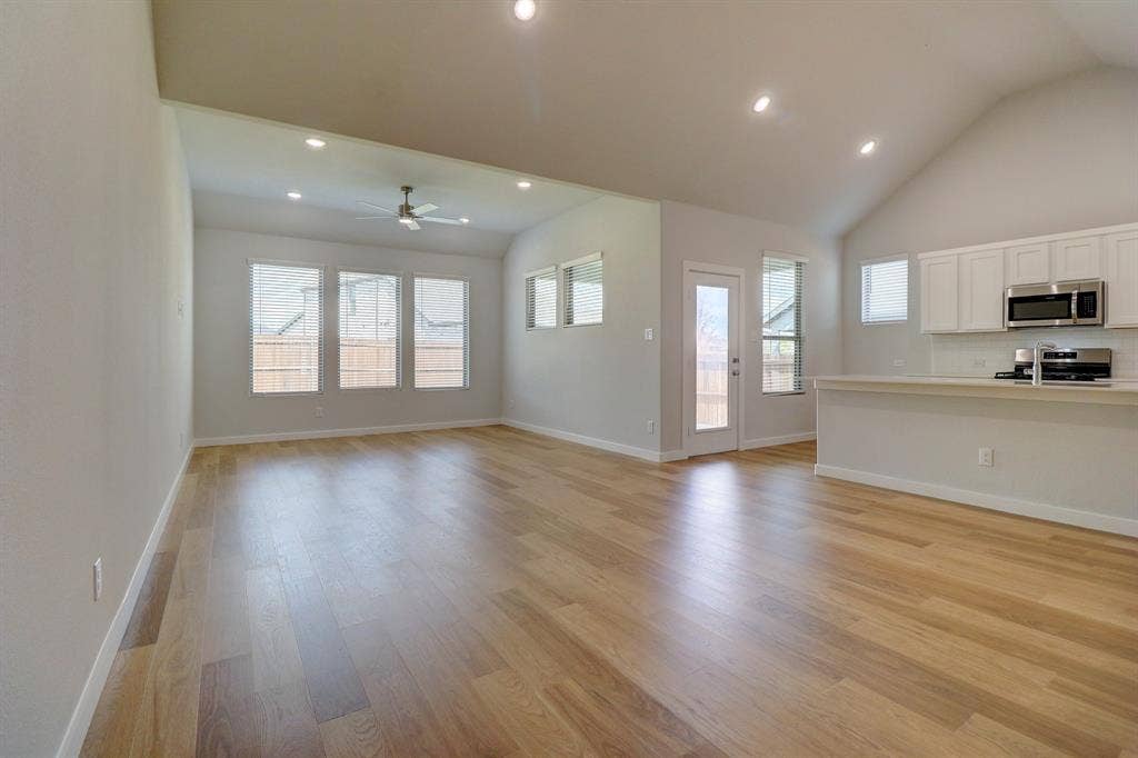 Vaulted ceiling with recessed lighting, wood-finish flooring, multiple windows, kitchen with white cabinetry, and stainless steel appliances