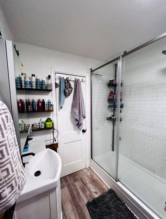 Tub and shower combination with subway tile surround, clear glass enclosure, modern vanity with vessel sink, and wood-finish flooring