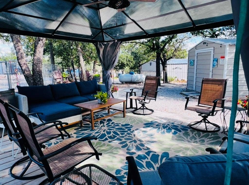 Covered patio structure with a ceiling fan, wood-finish decking, and a gravel yard with a storage shed