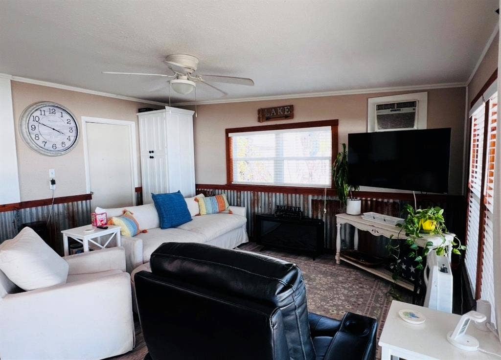 Corrugated metal wainscoting, a ceiling fan with integrated lighting, a built-in window air conditioning unit, and multiple windows with blinds