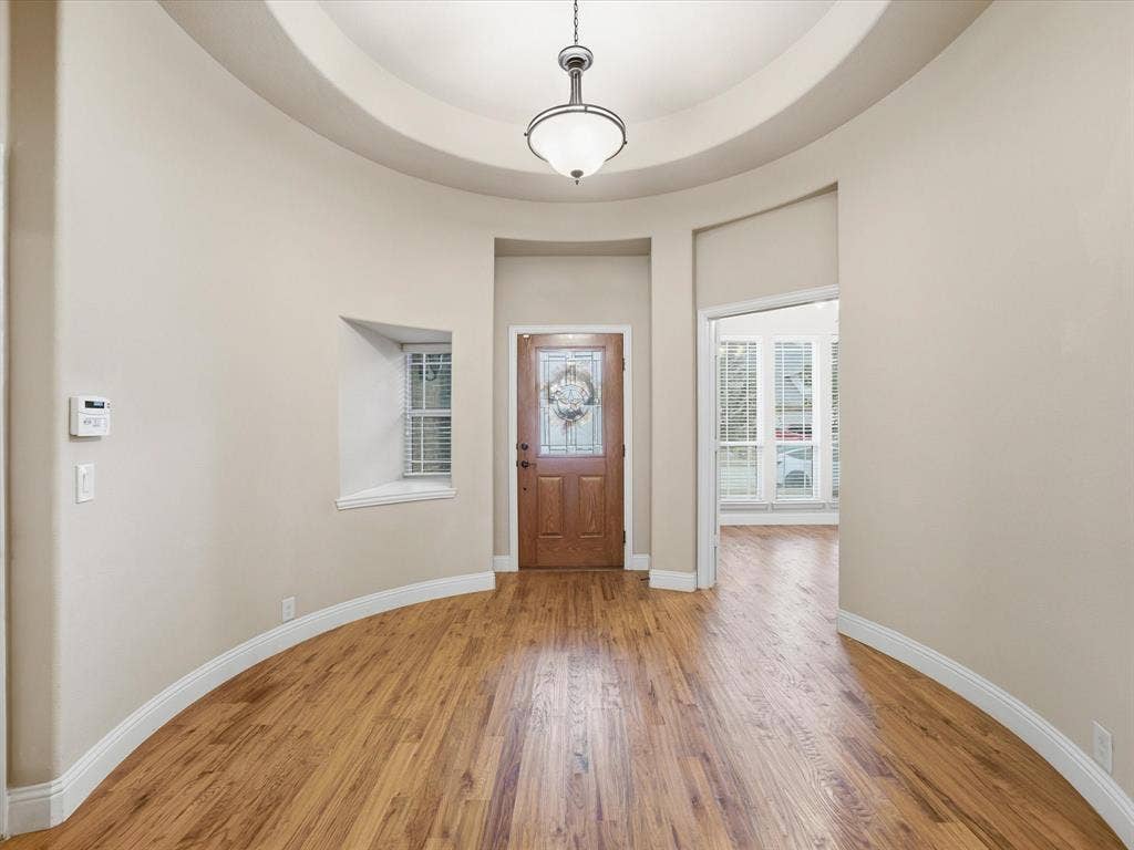 Circular foyer featuring wood-finish flooring, a domed ceiling, recessed window niche, and a central pendant light fixture with a glass-paneled wooden entry door