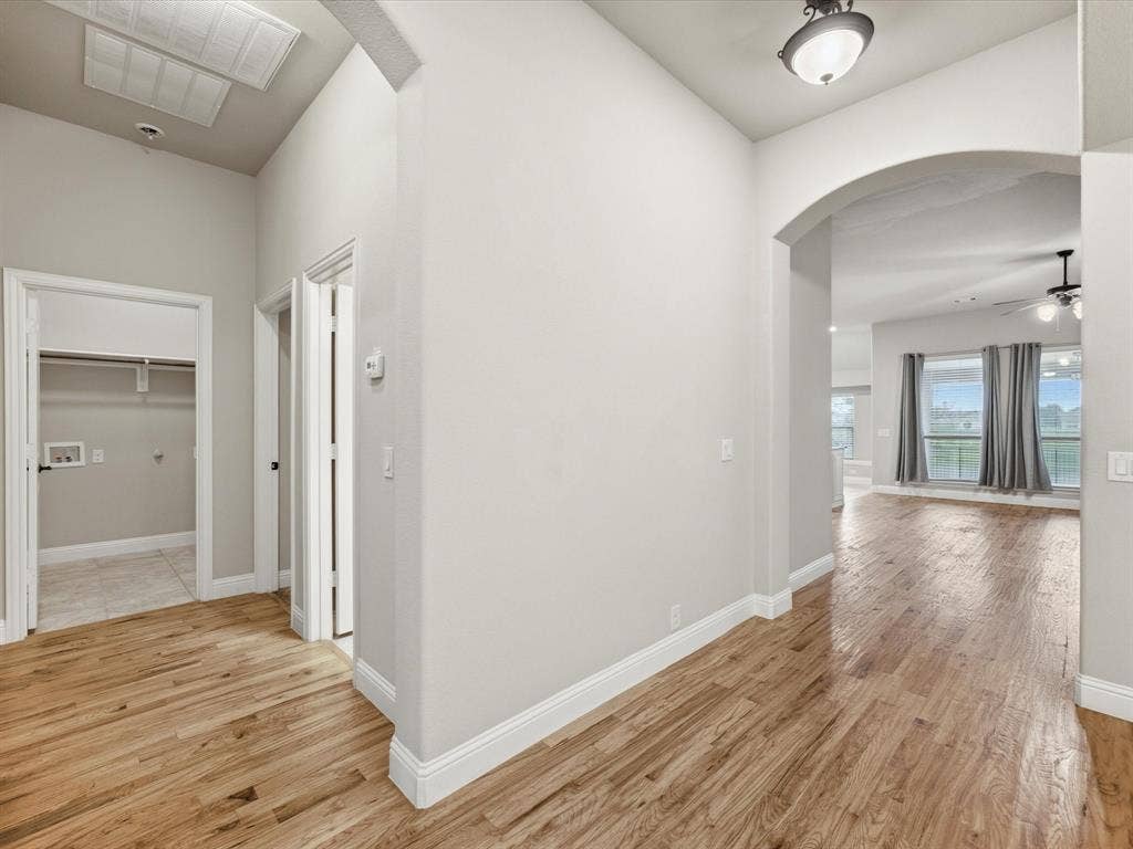 Interior hallway featuring wood-finish flooring, high ceilings, arched architectural detailing, and a dedicated laundry area with tile flooring